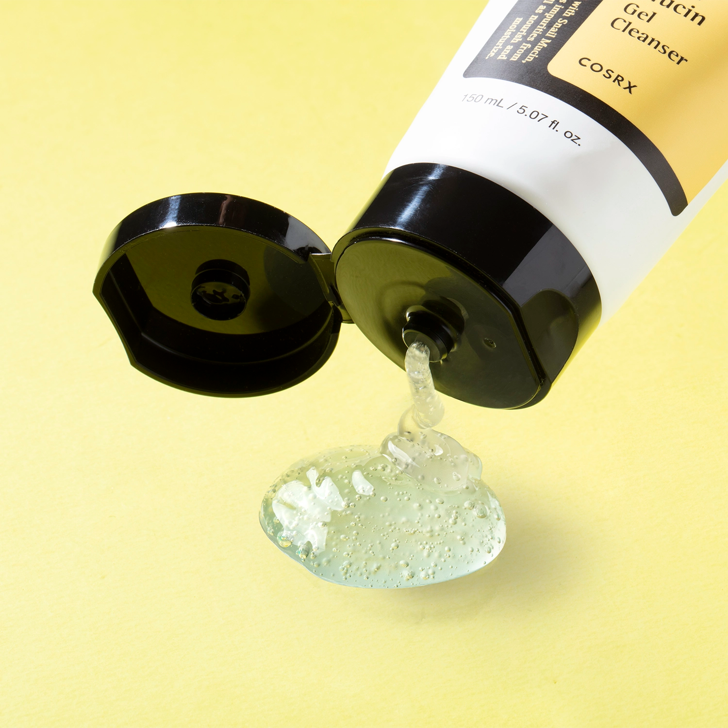 Gel nettoyant au mucin d’escargot en tube, déversant une goutte épaisse translucide sur fond jaune.