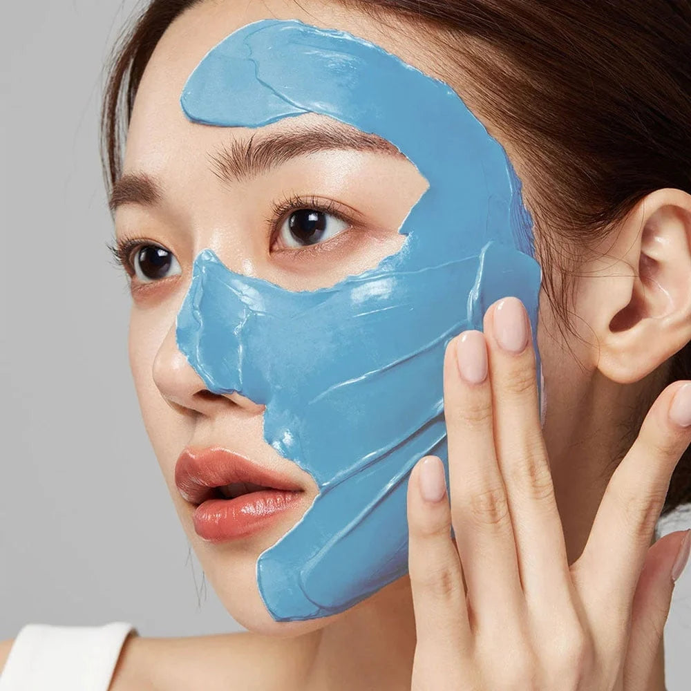 Masque facial bleu malaxé en feuille sur le visage d’une femme, peau lisse et yeux ouverts, dépeau et contour net.